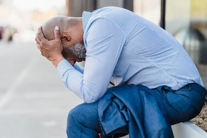 A distressed man sitting outdoors holding his head in hands, coping with difficulty before divorce.
