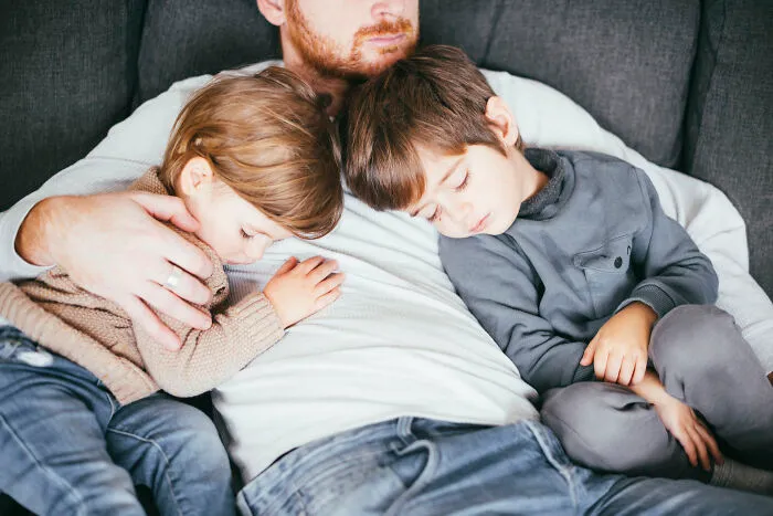 A father napping on a couch with his two young children