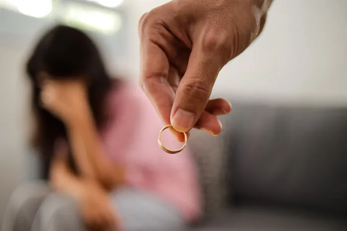 A hand holding out a wedding ring to a crying woman, representing divorced people and broken relationships.
