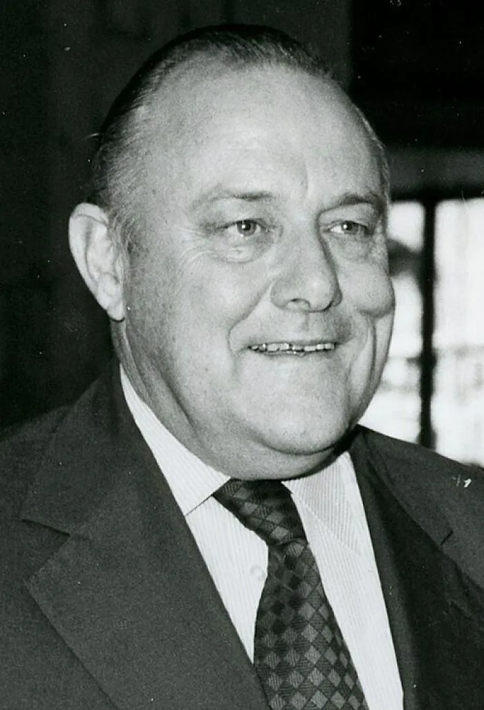 A black and white portrait of a smiling older man, illustrating clever wit and intelligent insults.