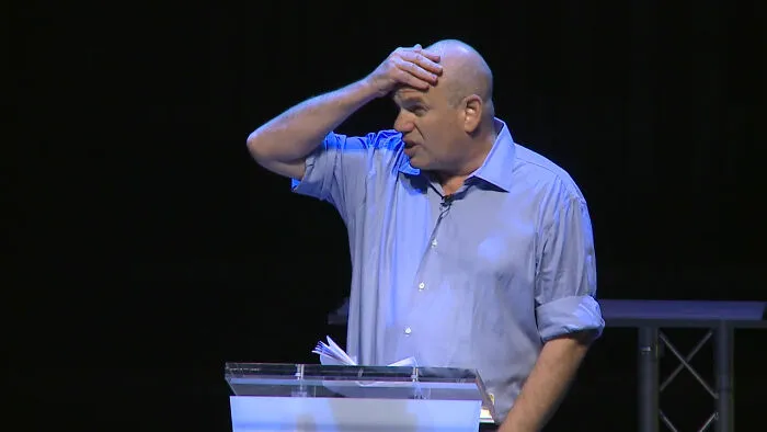A man on stage touching his forehead in confusion, reacting to intelligent insults