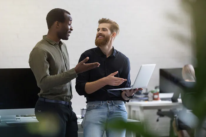 Two male colleagues discussing work on a laptop, perhaps sharing intelligent insults.