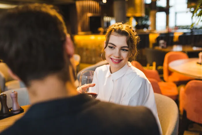 A woman smiling subtly at a man over dinner, hinting at intelligent insults.