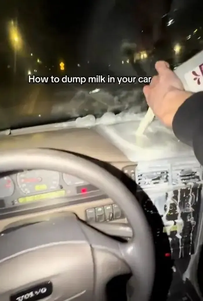 Person dumping milk onto car dashboard causing a mess
