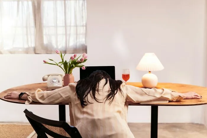 An exhausted woman rants with her head resting on a desk next to a laptop.