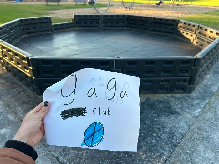 Hand holding a handwritten gaga club note near a playground pit, an example of found paper