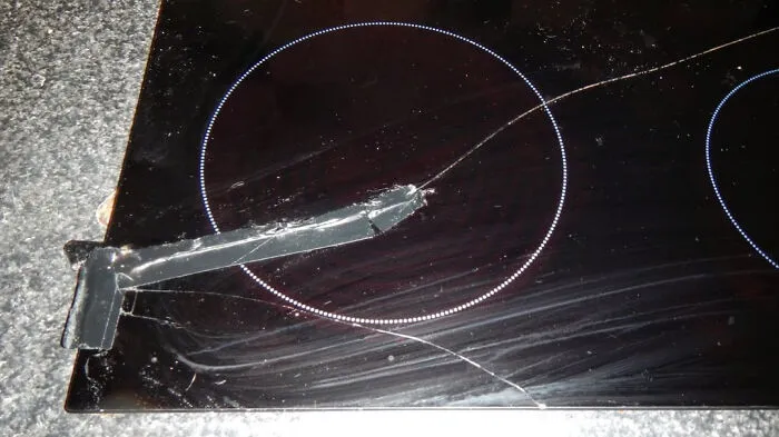 A cracked black glass stovetop taped together with black duct tape, depicting a home renovate fiasco