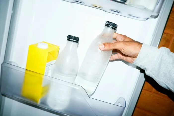 Hand placing a frosted bottle inside a fridge door with other beverages