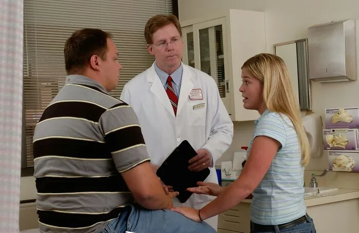 Doctor listening to woman and man in medical exam room