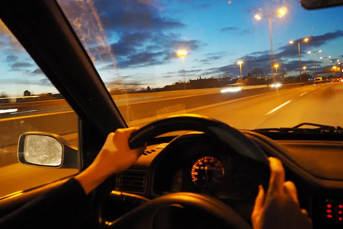 Hands on a steering wheel driving at night to leave after seeing red flags in someone's home