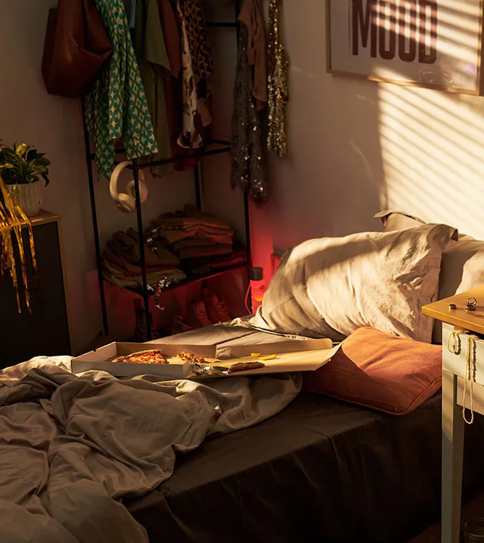 A messy bedroom with an open pizza box on the bed, representing gross things spotted in someone's home.