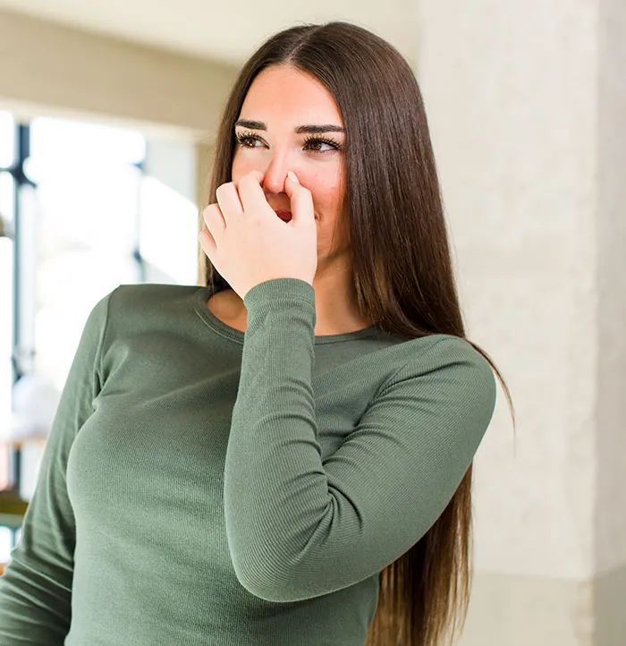 A woman holding her nose from a foul smell, illustrating unsettling things spotted in someone's home.