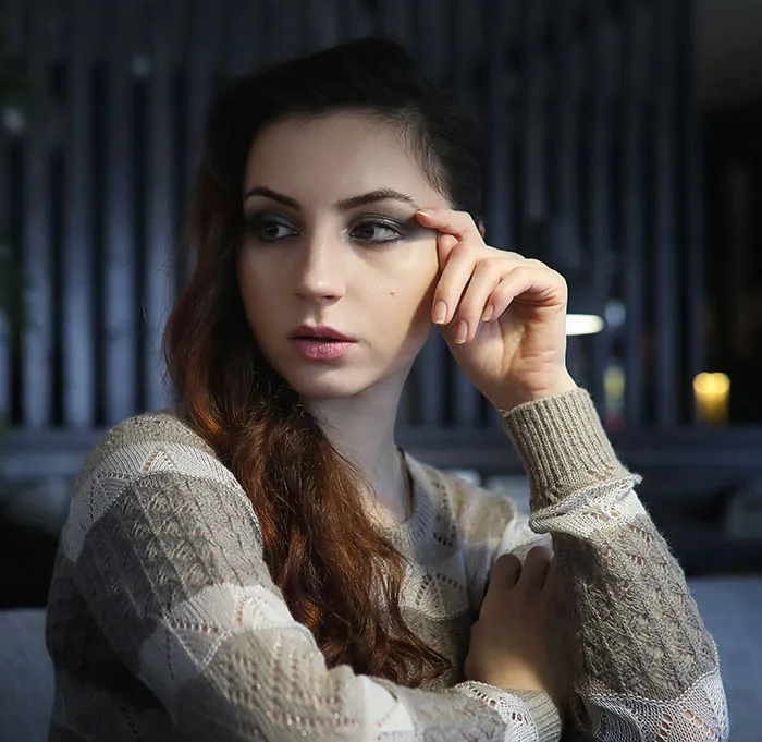 A thoughtful young woman sitting in someone's home with a hand near her temple.