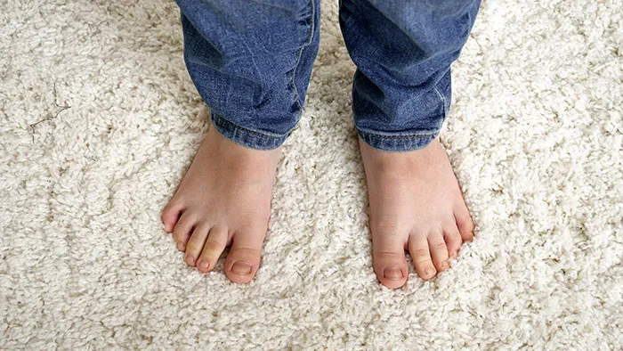 Bare feet standing on a soft white shaggy rug in someone's home.