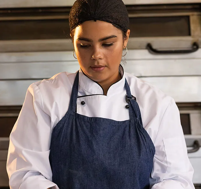 A female chef in a white uniform looking down thoughtfully in someone's home kitchen.