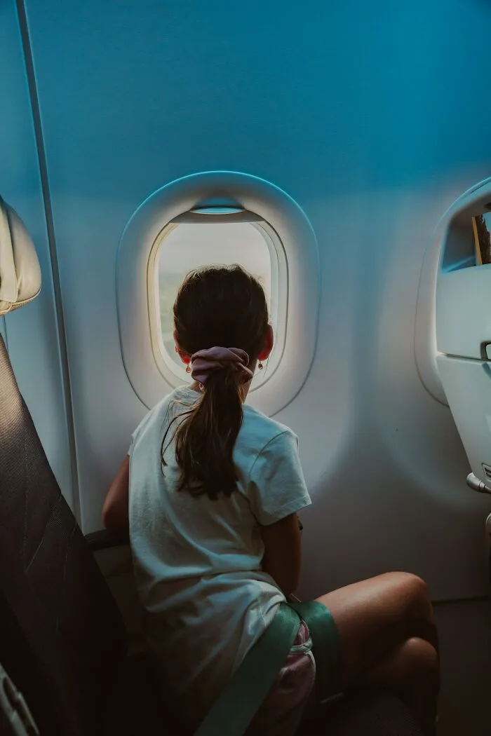 A young girl sits by an airplane window looking out during flights