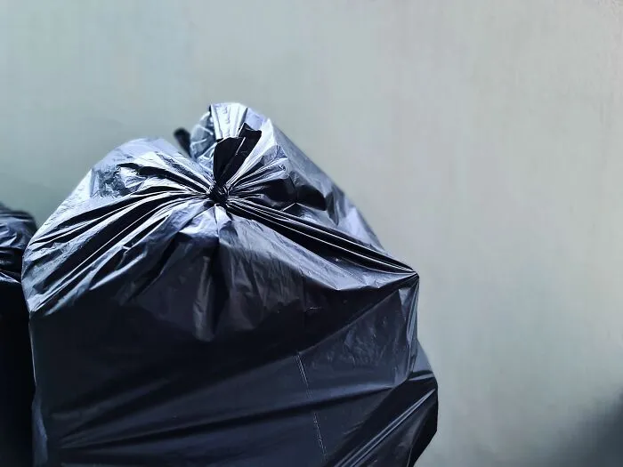 A tied black trash bag sitting outdoors in a tiny community area.