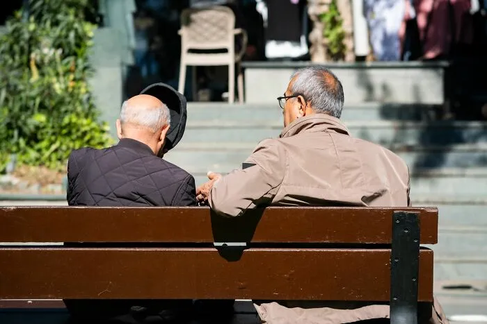 Two elderly men sitting on a park bench talking in tiny communities drama