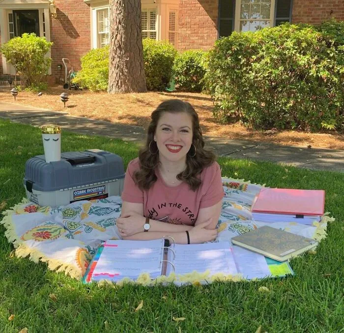 A perfectly confusing photo of a woman sitting outdoors on a blanket with books and a face mug.