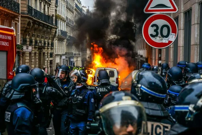 Police officers near vehicle on fire during urban chaos