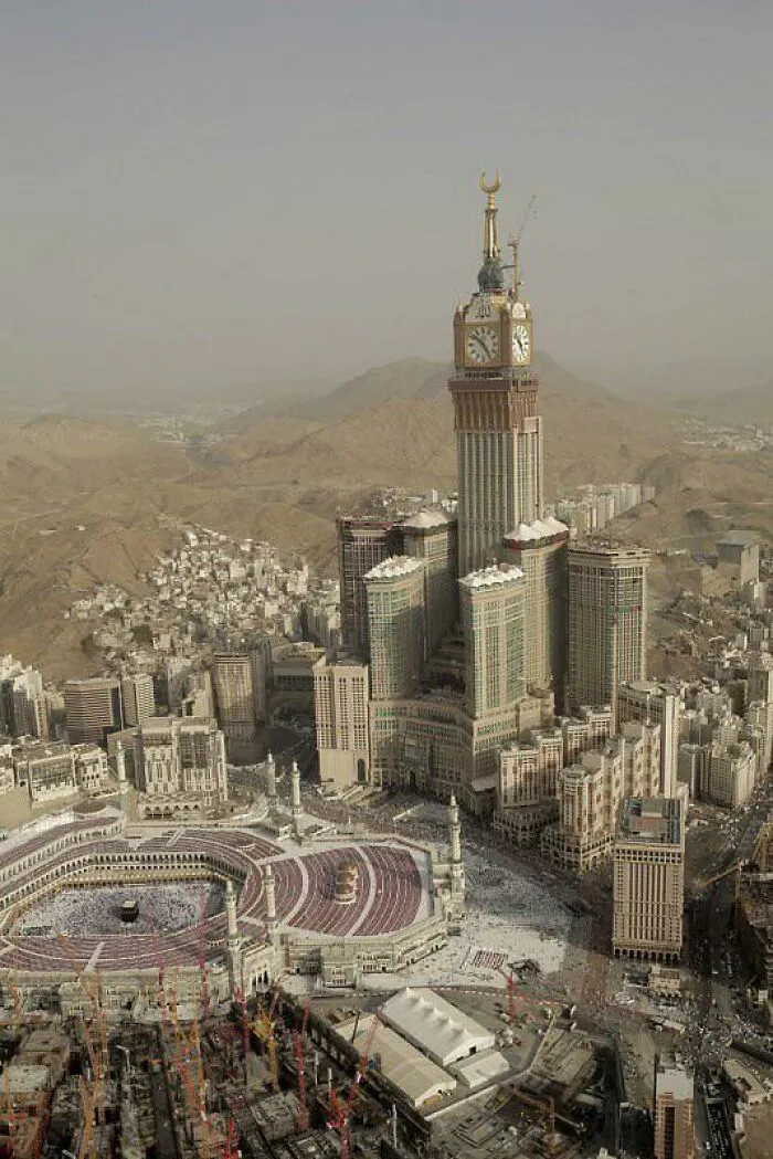 Tall clock tower with golden crescent spire overlooking city and desert