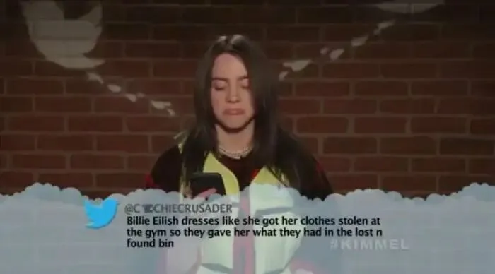 Billie Eilish reading funny insults about her clothing style during a TV show segment.