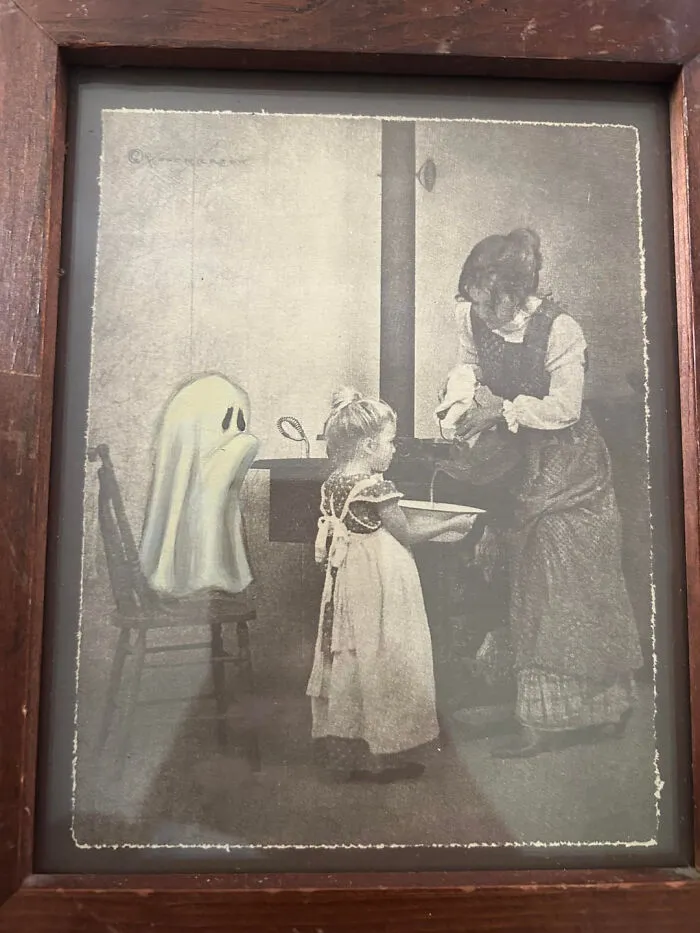 A framed vintage black and white print featuring a cute sheet ghost interacting with children for Halloween.