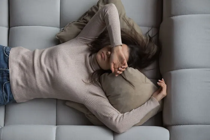 A woman lying on a sofa with her arm over her face, highlighting chronic health problems.