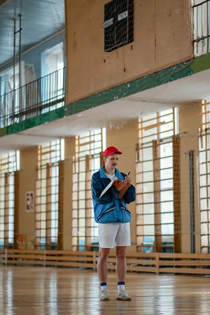 Physical education teacher in a gym writing on a clipboard, recalling classic school rumors about teachers.