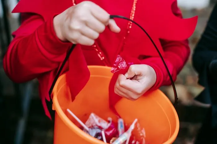Child in costume holding an orange bucket filled with candy while trick-or-treating.