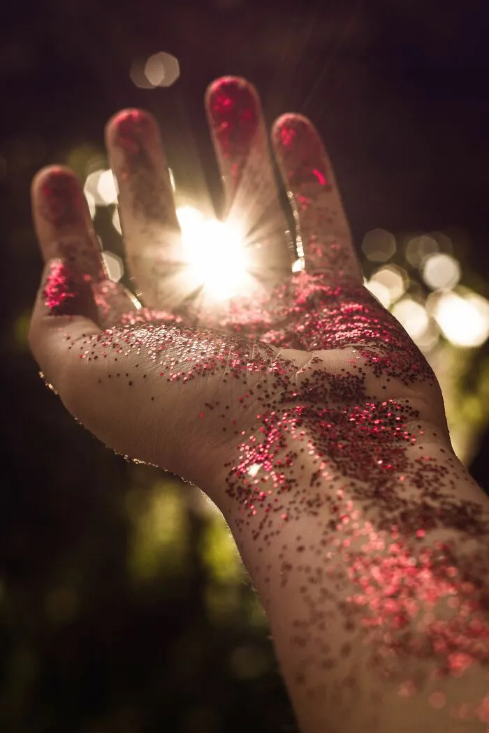 Hand covered in red glitter with sun rays shining through fingers