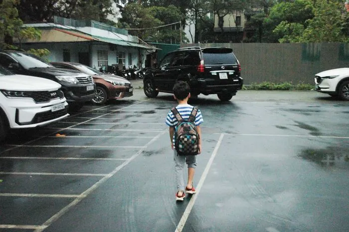 Young boy walking alone in parking lot with backpack