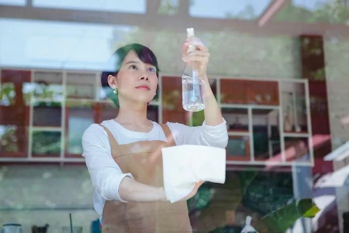 A woman spraying cleaner and wiping window glass, illustrating challenges faced by an Airbnb Host.