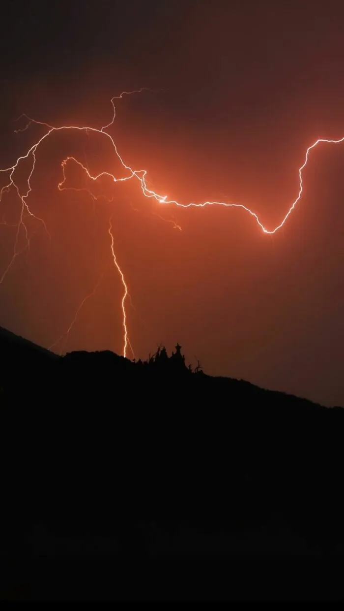 Bright orange lightning striking over a dark mountain, showing a stormy night that makes people leave immediately.