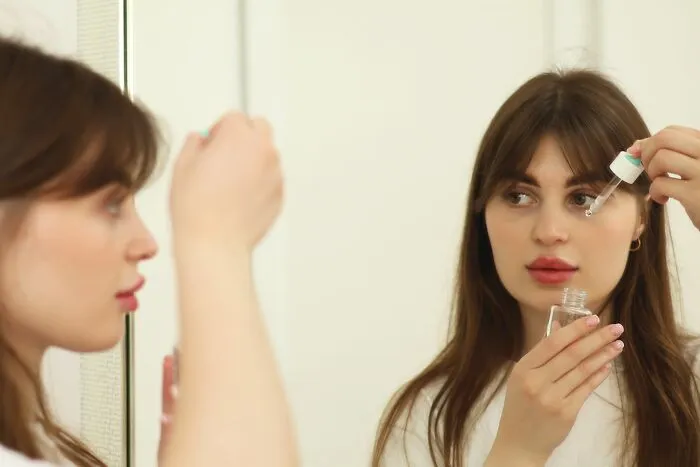 A young woman applying serum to her face in front of a mirror with brilliant tips for skincare