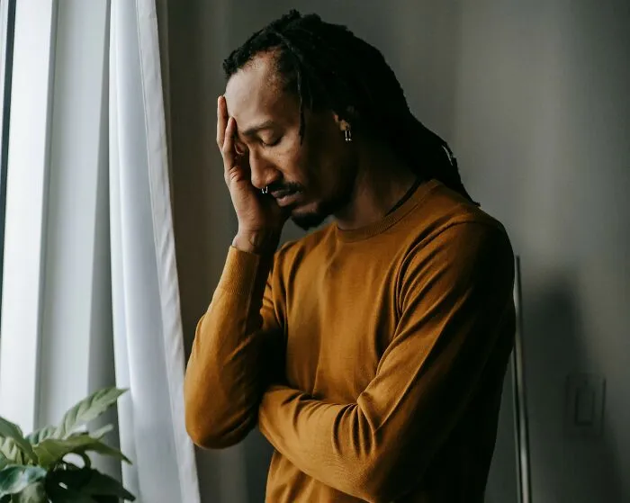 A man with dreadlocks holding his head in stress, representing deep personal secrets.