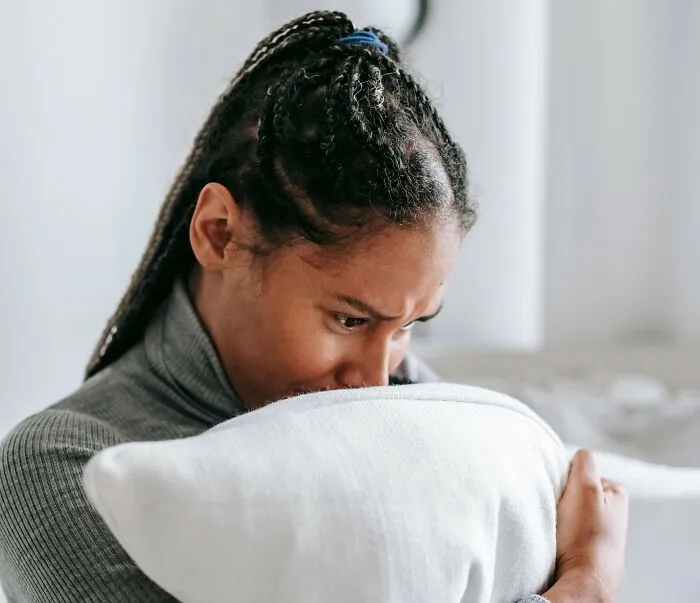 A woman hugging a pillow while holding back deep emotional secrets.