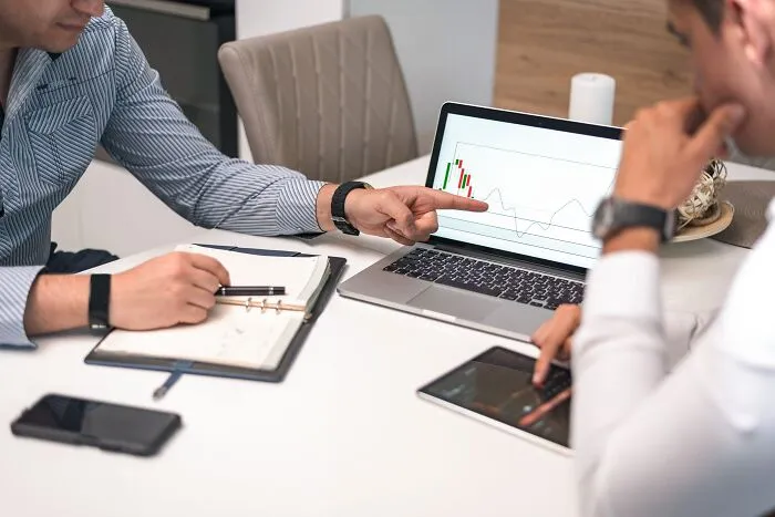 Two colleagues analyzing financial charts on a laptop after a costly slip-up leading to a massive bill
