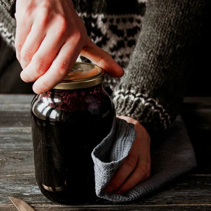 Hand using cloth to grip and open a jar lid on a wooden table