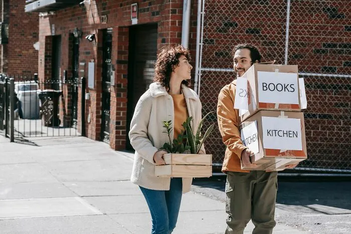 A couple carrying moving boxes, discussing things that made them question their intelligence.