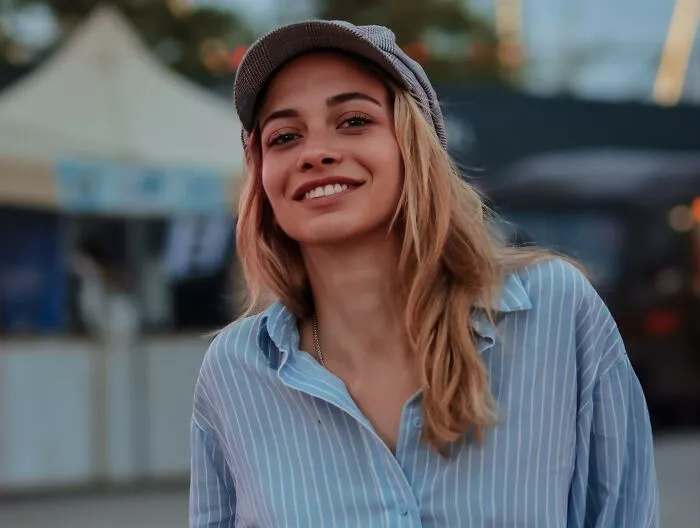 A smiling woman wearing a flat cap and striped shirt outdoors, keeping hidden secrets to herself.