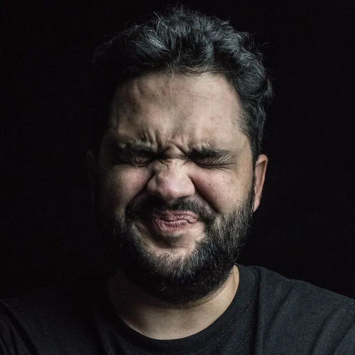 Close-up of a man grimacing with eyes squeezed shut, illustrating satisfying revenge stories