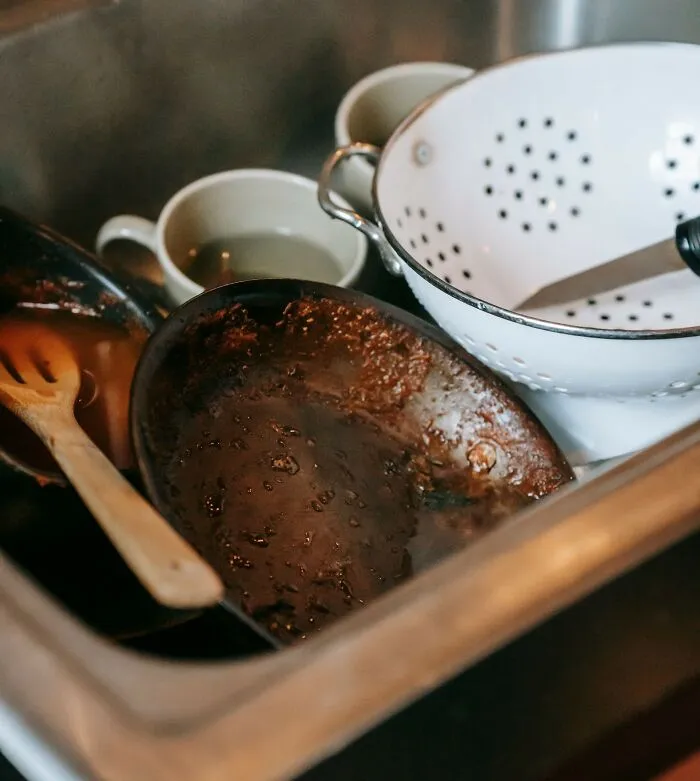 Dirty dishes and utensils piled in sink, showing unwashed kitchen mess