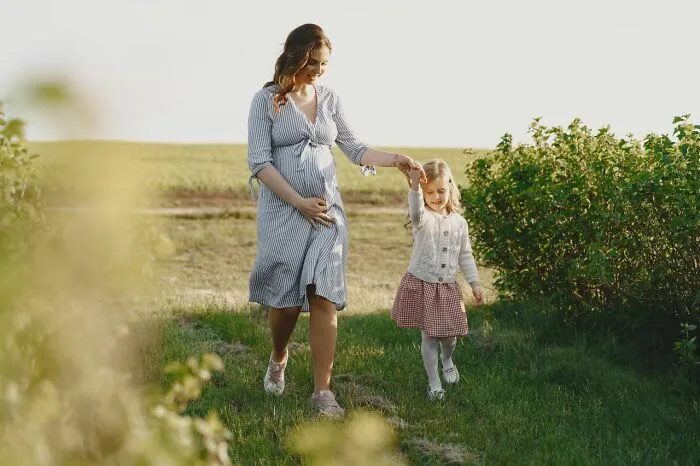 Pregnant mother walking with her daughter in a field, sharing classic school rumors of her youth.