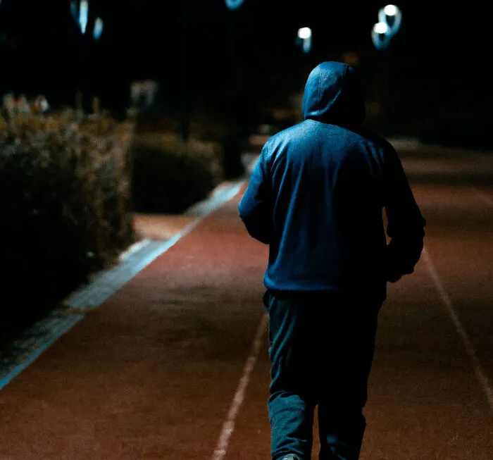 Person in a blue hoodie walking at night, linked to satisfying revenge stories.