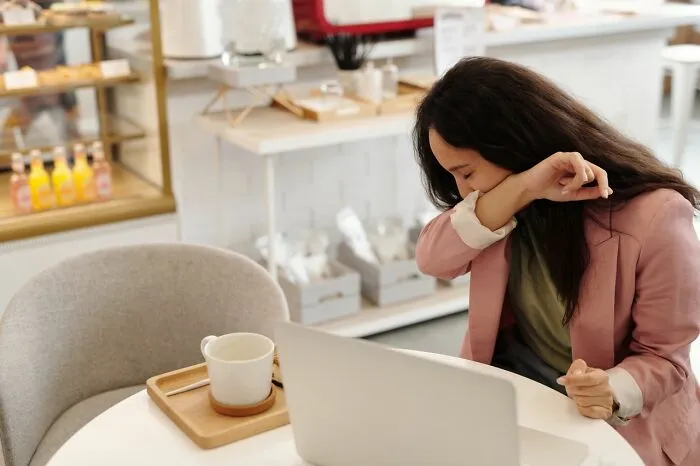Woman coughing into elbow while working at laptop practical life hacks