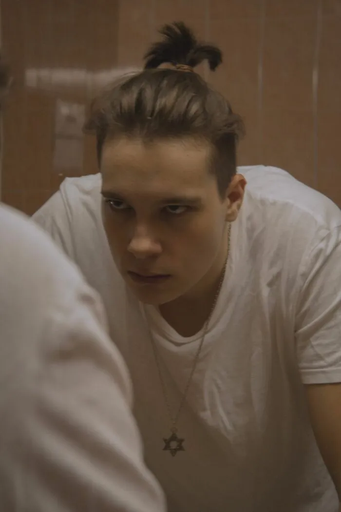 A young man with a hair bun looking in a mirror applying clever life tricks