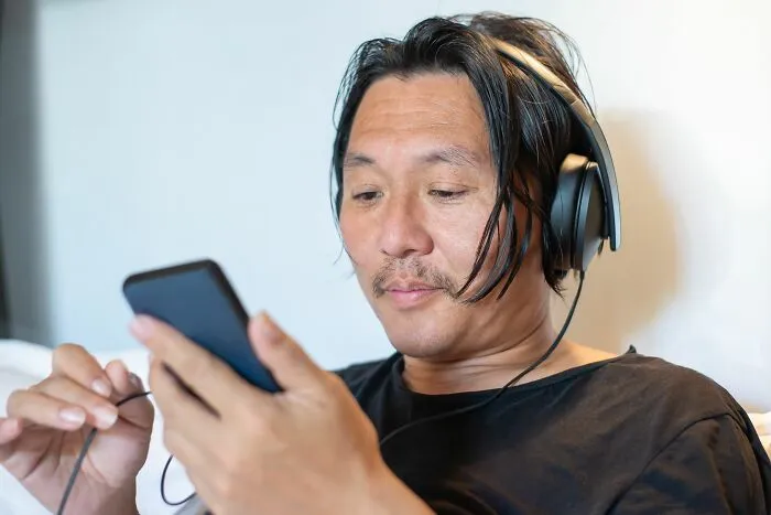 A man wearing headphones using his phone, listening quietly to secrets he keeps from people in his real life.