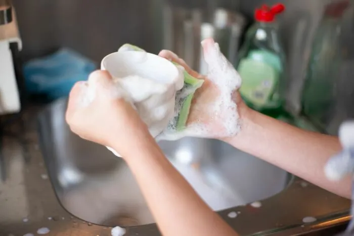 A person washing a white cup with a sponge in the sink, showing simple everyday life tips.