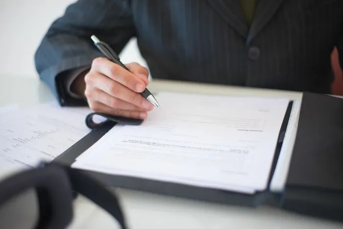 A person in a business suit holding a pen over official documents, hinting at a school rumor investigation